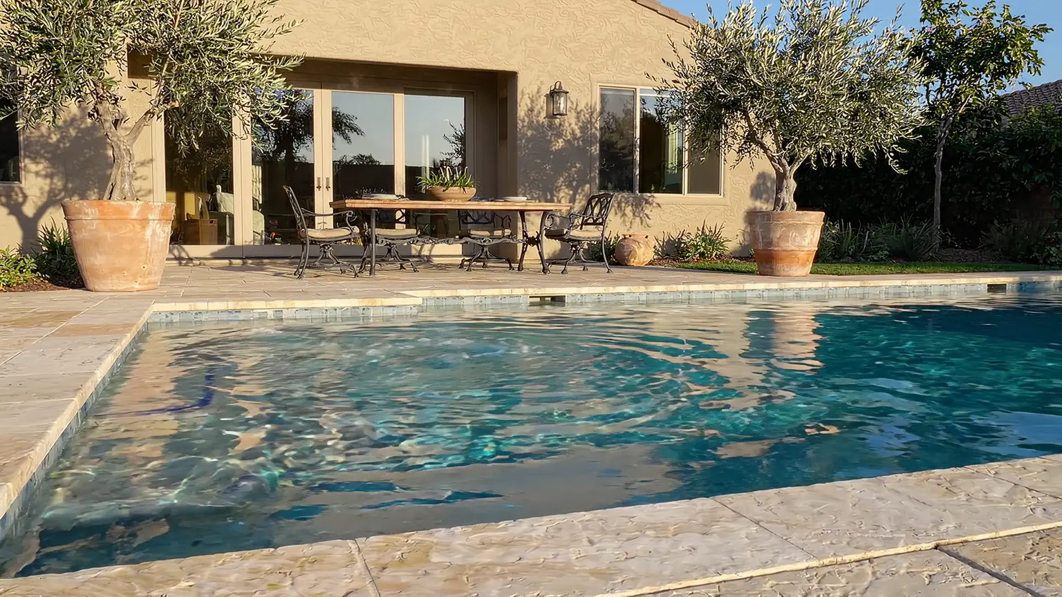Residential pool with shallow steps and pale stone coping beside a stucco home